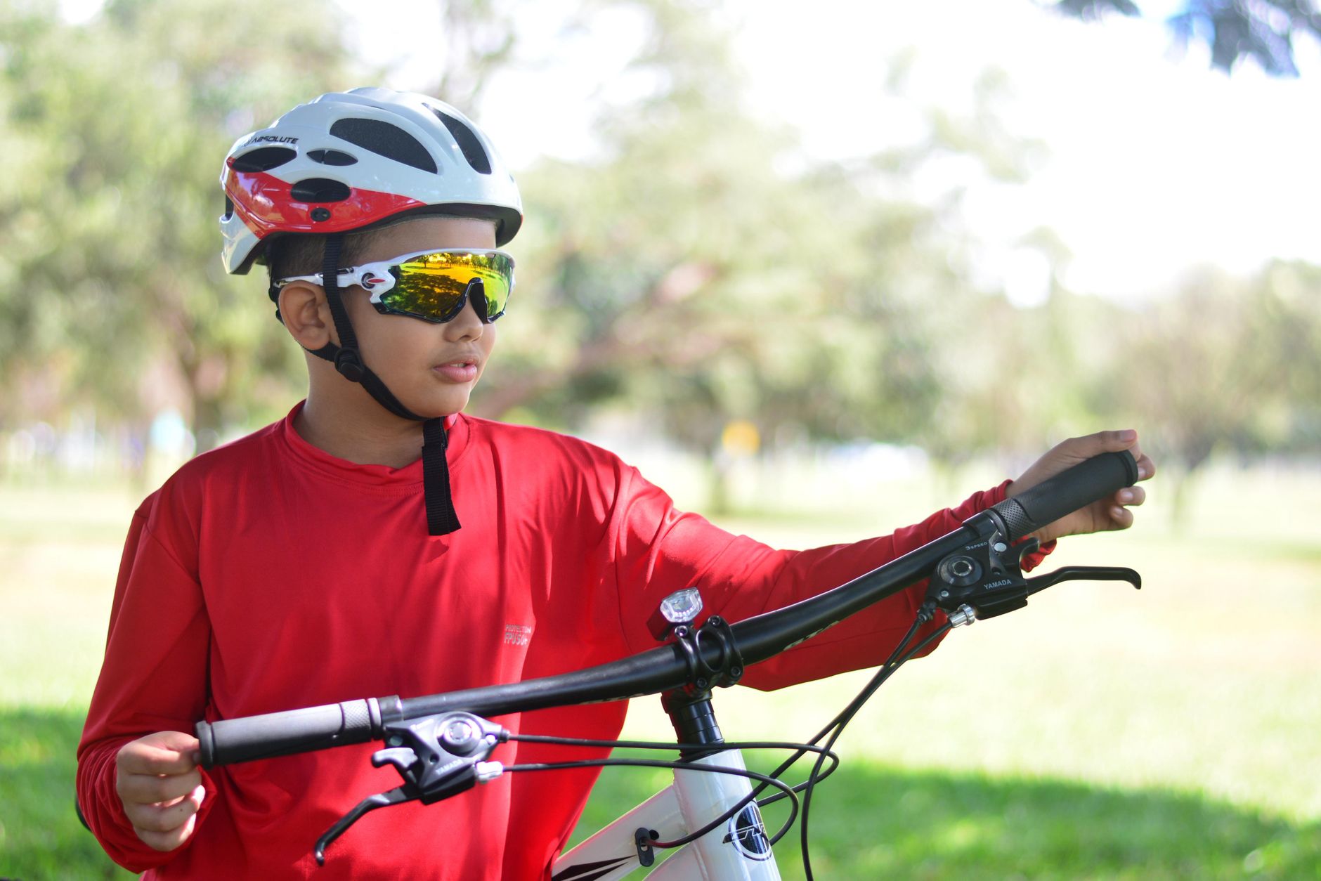 Teen cyclist wearing helmet and sunglasses, riding outdoors in a park setting. — illustrating What Are Sports Sunglasses Built Differently For?