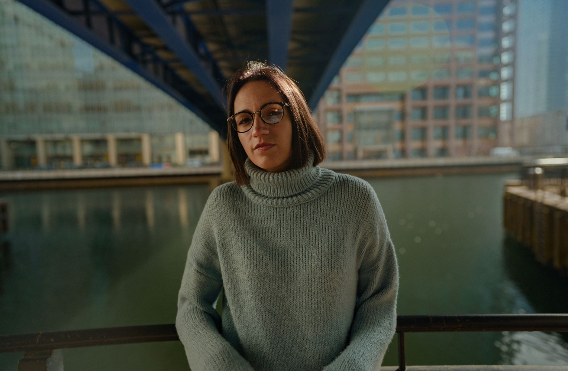 Woman wearing eyeglasses and sweater posing near an urban canal under a bridge. — illustrating What Is a Double Bridge, and Is It Purely Decorative?