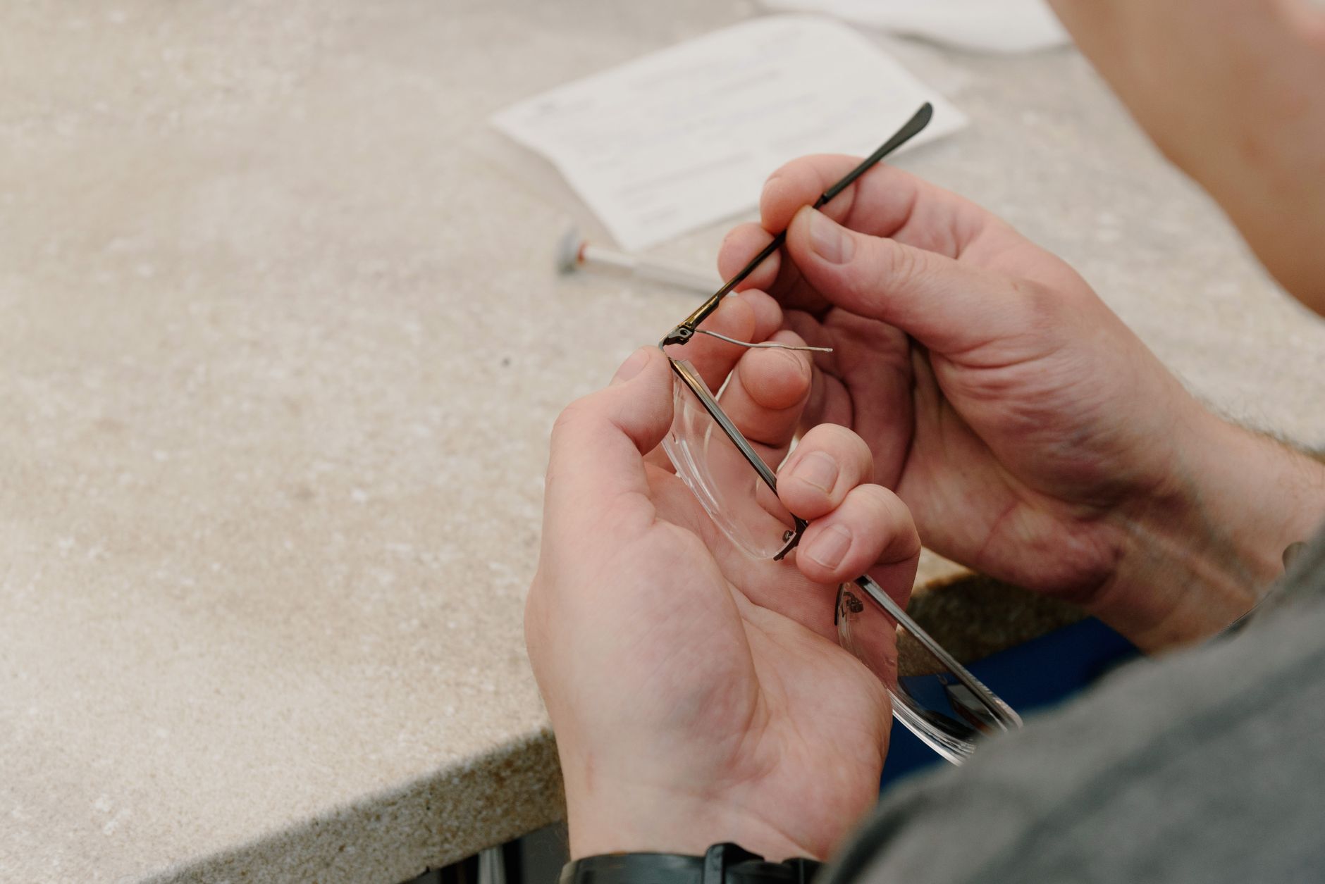 From above of anonymous male master sitting at table and fastening temple with screw while repairing eyeglasses in professional workshop — illustrating What Is a Screwless Hinge, a