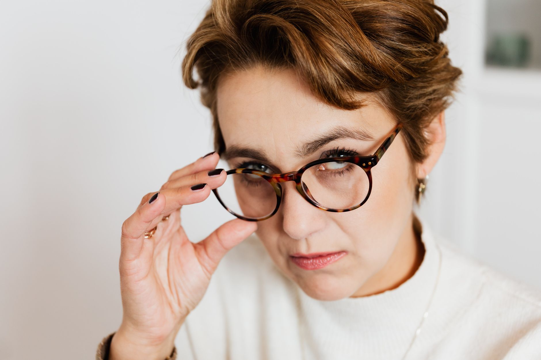 An expressive close-up portrait of a woman adjusting her eyeglasses, conveying contemplation. — illustrating Where Did the Tortoiseshell Pattern on Glasses Come From?