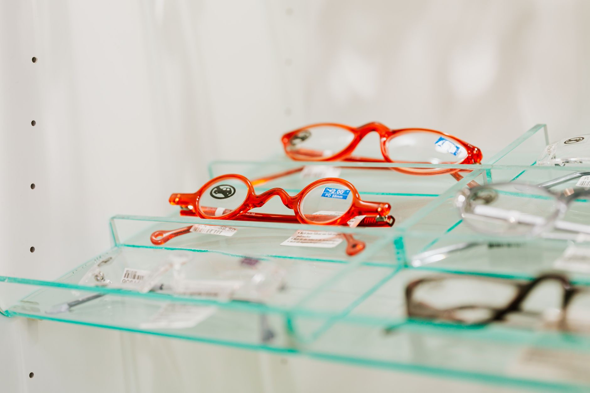 Stylish red eyeglasses displayed on a glass shelf in an eyewear store. — illustrating Why Clear and Translucent Frames Look Different on Everyone