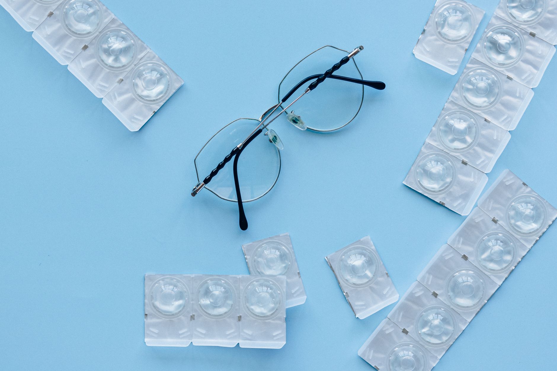 Eyeglasses and contact lenses on a blue background. Concept of eye care and vision correction. — illustrating Why Strong Prescriptions Make Eyes Look Bigger or Smaller